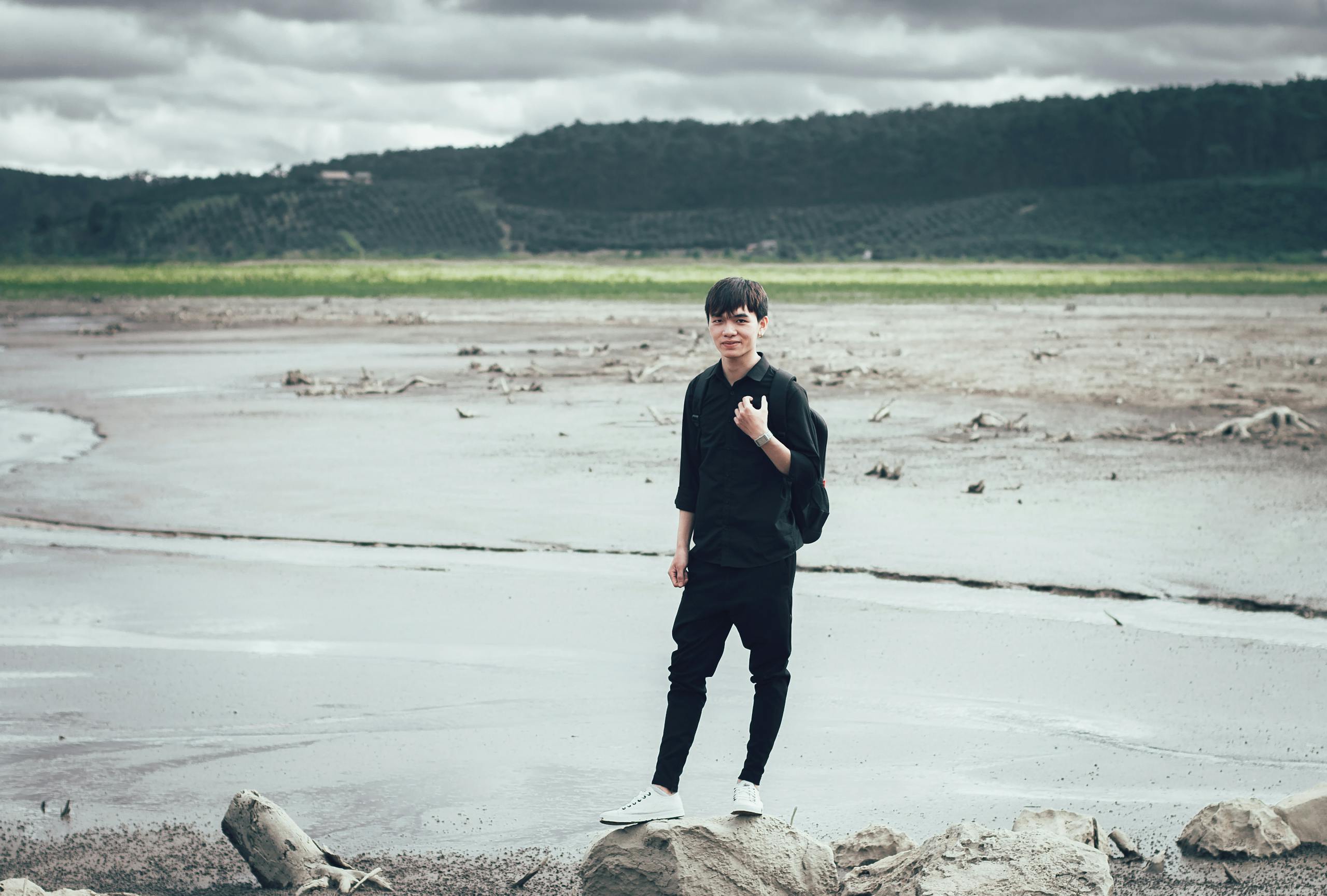A young man stands confidently on a desolate landscape, surrounded by nature.